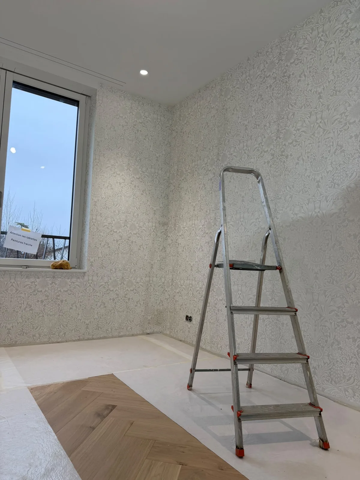 Pose de papier peint en cours, escabeau au centre de la pièce